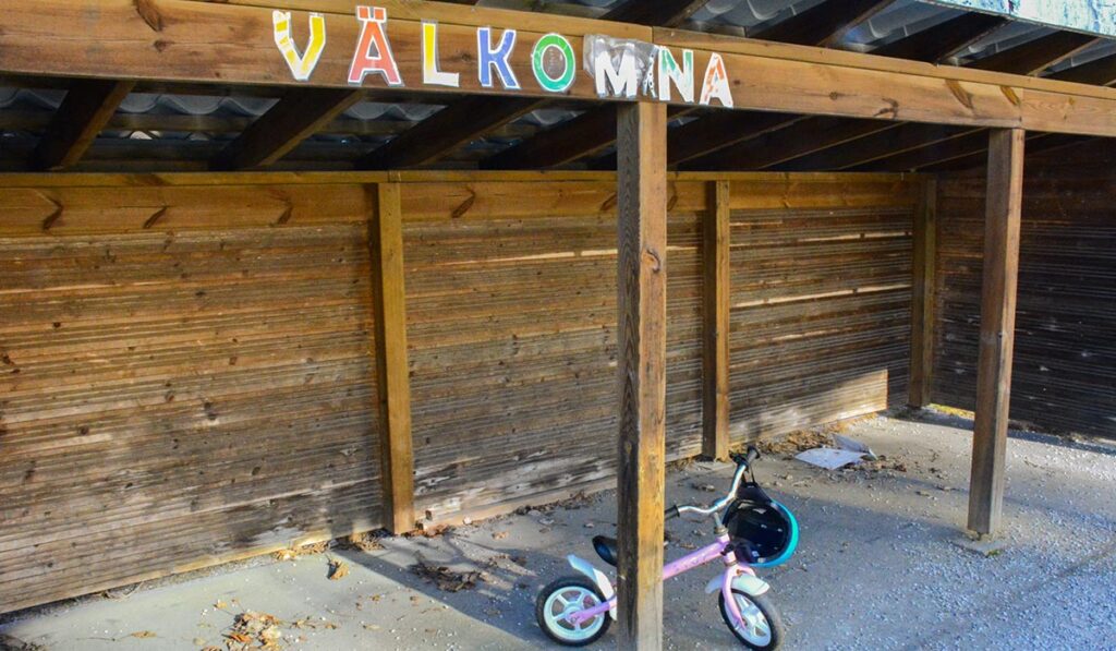 en cykelbrack med ordet VÄLKOMNA i färglagda bokstäver på toppen. På botten står en ensam barncykel