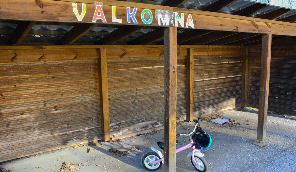 en cykelbrack med ordet VÄLKOMNA i färglagda bokstäver på toppen. På botten står en ensam barncykel