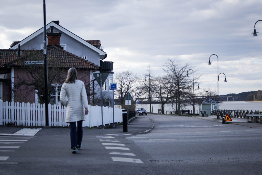 En ensam kvinna som går över en väg, till höger ser man en ensam bil kommande mot kameran